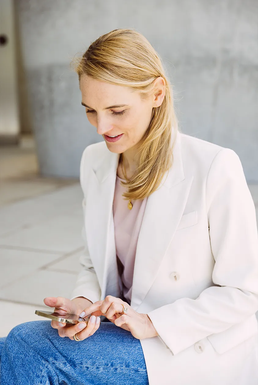 Dies ist ein Bild von Life, Business und Health Coach Dr. Kirsten Schlömer. Es zeigt sie in Seitenansicht mit Blick auf ihr Mobiltelefon.